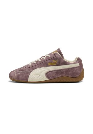 Zapatilla Puma de ante púrpura con raya de logo blanca, cordones blancos, texto Puma dorado y suela de goma marrón, mostrada de lado sobre fondo blanco.