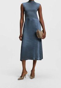 Šaty bez rukávů, přiléhavý korzet v tmavě modrém saténu s rozšířenou sukní. V kombinaci s nahými lodičkami a malou, elegantní kabelkou.