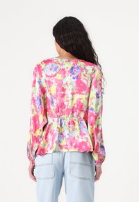Top peplum floreale nei toni del rosa, giallo e blu. Tessuto leggero con maniche lunghe, vita elasticizzata e vestibilità ampia. Dettaglio sulla scollatura posteriore visibile.