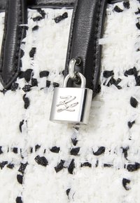 Sac en tweed avec une texture blanche et noire. Accents en cuir noir et détail de verrou en argent avec logo gravé à l'avant.