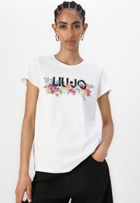 T-shirt en coton blanc à manches courtes, avec un motif floral et le texte "LIU-JO" en noir. Texture douce avec une coupe décontractée.