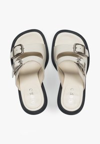 Beige slide sandals with two wide straps and metallic buckles, featuring a smooth synthetic upper and a black rubber sole.