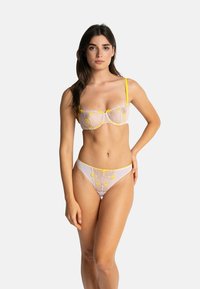 Ensemble de lingerie en dentelle comprenant un soutien-gorge blanc transparent avec broderies jaunes et une culotte assortie. Les bretelles sont fines avec des accents jaunes.