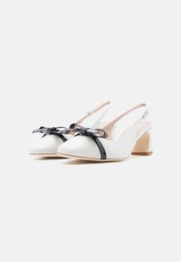 Witte slingback hakken met een puntige neus, voorzien van een zwarte glanzende band en strikdetail. Gestructureerde afwerking met een lichtbeige binnenkant.