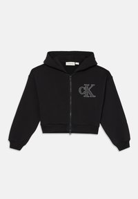 Crna skraćena dukserica od mekog materijala, s patentnim zatvaračem sprijeda, kapuljačom i sjajnim "cK" logotipom na prsima. Rebrasti manžeti i donji rub.
