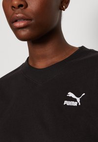 Felpa nera in cotone con scollatura a V e logo Puma bianco. Presenta maniche corte e una texture morbida e liscia.