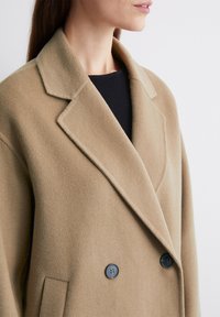 Beige wollen blend jas met een notchkraag, dubbelgeknoopte knopen en een zachte textuur. Beschikt over zijzakken en een getailleerde pasvorm.