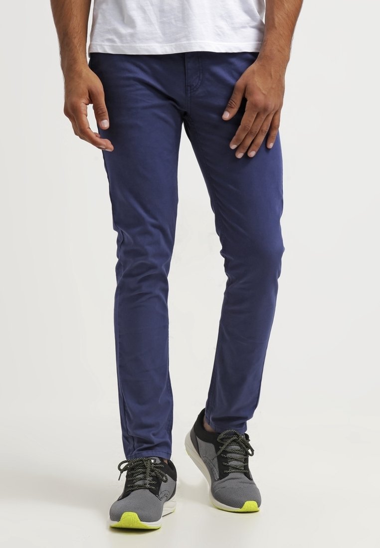 Navy blue slim-fit pants made of cotton blend, featuring standard pockets and a smooth texture, paired with black and gray sneakers with yellow accents.