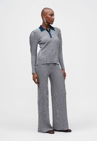 Costum din două piese cu dungi în nuanțe de albastru închis și alb. Top cu mâneci lungi și guler, cu accente verzi, pantaloni evazați. Textura materialului este netedă.