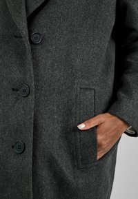 Abrigo de lana gris oscuro con cuello con muesca, seis botones negros y un bolsillo lateral. La textura parece suave y ligeramente difusa.