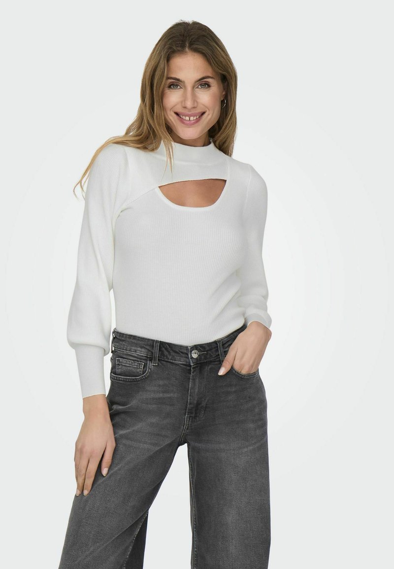 Weißer gerippter Pullover mit hohem Kragen und Ausschnitt, kombiniert mit dunkelgrauen Jeans mit hoher Taille im klassischen Schnitt.
