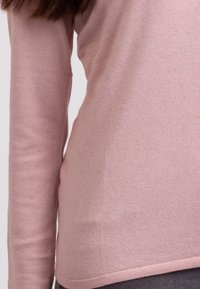 Růžový pletený svetr s dlouhými rukávy, texturovaná tkanina, přiléhavý design a kulatý lem. V kombinaci s přiléhavými tmavými kalhotami.