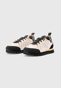 Helle rosa Stoff-Sneaker mit schwarzen Gummi-Akzenten, strukturierten Sohlen, goldenen Ösen und einer Rückenzugschlaufe. Mit horizontalen Nähdetails.