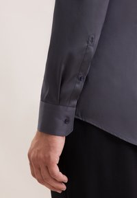 Donker marineblauw overhemd met knopen en een gladde, glanzende textuur. Heeft een puntige manchette en twee bijpassende knopen voor een veilige sluiting.