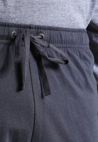 Nærbillede af mørkegrå sweatpants med en snøret talje, der bæres over en gråstribet skjorte.