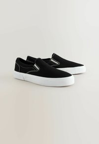 Schwarze Leinenschlupfschuhe mit weißen Gummisohlen und kontrastierenden weißen Nähten, ausgestattet mit leichter Elastik für ein einfaches Anziehen.