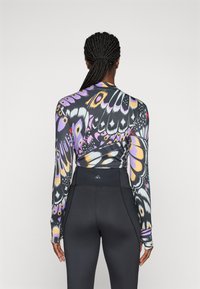 Tricou de antrenament cu mânecă lungă, cu imprimeu de fluturi în violet, negru și galben, combinat cu colanți negri cu talie înaltă, care au detalii cu logo.