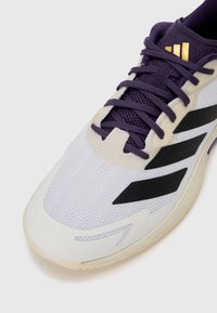 Adidași sport albi și mov, din material mesh, cu trei dungi negre, șireturi în mov corespunzător, talpă din cauciuc neted și accente aurii.