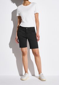 Černé šortky s kapsou na zip, doplněné jednoduchým bílým tričkem. Outfit je doplněn bílými teniskami. Čistý design a střih.