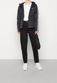 Svart pufferjacka med huva, med vita randiga detaljer på ärmarna. Matchad med svarta högmidjade byxor och vita sneakers.