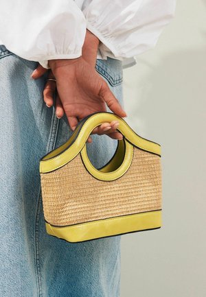 Pequeña bolsa estructurada con un cuerpo de paja tejida, acentos de cuero amarillo y un asa curvada. Presenta un ribete negro contrastante.