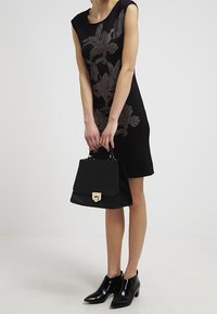 Black dress with floral metallic embroidery, knee-length, paired with a structured black bag and shiny black ankle boots.