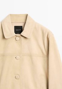 Beige ruskindsjakke med en klassisk krave, to knapper foran og synlige sømdetaljer. Mærket lyder "Massimo Dutti."