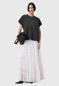 Maglione grigio scuro a maglia con maniche corte, abbinato a una gonna maxi bianca a strati. Una borsa in pelle nera e stivali neri a punta completano il look.