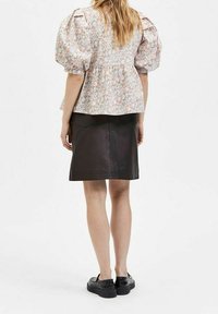 Blusa floreale con maniche a palloncino e vita cintrata, abbinata a una gonna in pelle nera aderente e sneakers nere, vista da dietro.