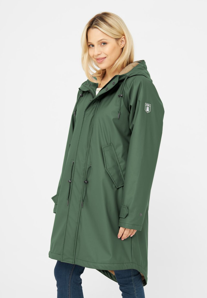 Parka impermeabile verde con cappuccio, vita regolabile con cordino, tasche frontali e fodera morbida. Presenta una toppa con il logo sulla parte superiore del braccio.
