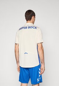 T-shirt de sport clair avec "SUPER BOCK" en bleu, à manches courtes, et un panneau latéral bleu. Assorti à un short bleu avec des accents blancs.