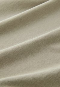 Lichtbeige stof met een gladde textuur, voorzien van subtiele vouwen en kreukels die wijzen op een zacht, rekbaar materiaal.