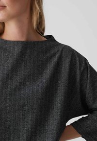 Zwart-witte top met een visgraatpatroon, een brede ronde hals en driekwartmouwen, gemaakt van gestructureerde stof.