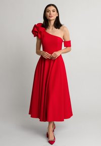 Czerwona sukienka na jedno ramię z dużym kwiatowym akcentem. Gładki materiał, dopasowana góra i rozkloszowany dół. Połączona z pasującymi czółenkami na szpilce.
