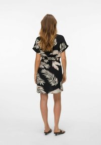 Abito nero con un motivo di foglie tropicali in beige e marrone scuro. Maniche corte, vita cintrata e design fino al ginocchio con una texture leggera.