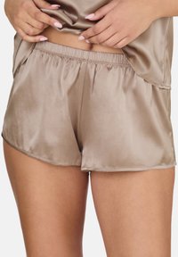 Svileni bež šortsevi s elastičnim pojasom, s glatkom teksturom, bočnim prorezima i blago zakrivljenim rubom za udoban fit.