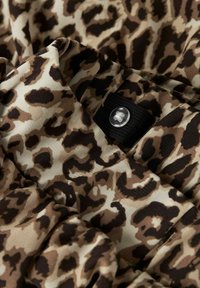 Leopardenmuster-Stoff, der eine Mischung aus Beige, Braun und schwarzen Flecken zeigt. Besitzt ein schwarzes Elastikband mit einem klaren Knopf zum Schließen.