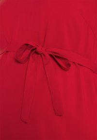 Abito in tessuto rosso con una cintura annodata come accento. Texture liscia, design semplice senza motivi, focalizzato su una dichiarazione di colore solido.