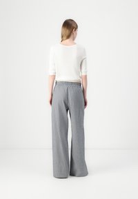 White cropped sweater with three-quarter sleeves paired with light gray, wide-leg striped trousers featuring an elastic waistband.
