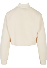 Lühendatud pullover pehmest kreemjaskangast, millel on kõrge kaelus ja pikad varrukad soonikservadega. Sile tekstuur ja minimaalne detailiseeritus.