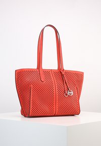 Sac fourre-tout en cuir rouge perforé avec doubles poignées, garniture noire contrastante et quincaillerie décorative arborant un logo.