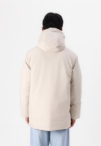 Helle beigen Steppjacke mit Kapuze, mit glatter Textur, lässigem Schnitt und abgesenktem Saum; geeignet für Freizeitbekleidung.