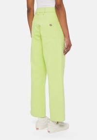 Vihreät puuvillaiset leveälahkeiset housut, joissa on kaksi takataskua ja merkkilogo. Mallilla on päällään valkoiset lenkkarit, joissa on teksturoitu pohja.