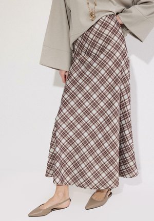 Femme portant un haut beige à manches larges, une jupe trapèze à carreaux marron et blanche, des ballerines beige à bride arrière et des colliers dorés superposés.