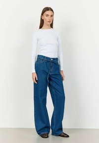 Jeans din denim blue, cu picioare largi și talie înaltă, cu închidere prin buton și tiv desfăcut. Asortat cu un top alb, ajustat, cu mâneci lungi.