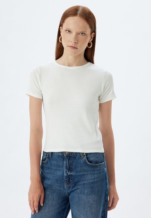 Camiseta blanca de manga corta con cuello redondo, combinada con jeans azul de cintura alta. Diseño simple, textura suave.