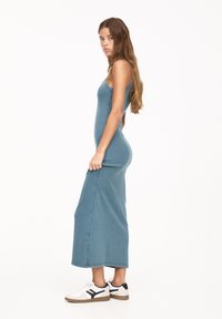 Rochie maxi din denim albastru cu un corpi ajustat și un tiv ușor evazat, asortată cu adidași albi cu accente negre și talpă bej.