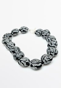 Collana di perle nere con perle tonde e motivi testurizzati in argento, tenute insieme da una chiusura, che mostra un forte contrasto di colori.