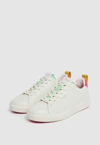 Zapatillas de cuero blancas con acentos en verde y rosa, punta redonda, diseño con cordones y una lengüeta de talón amarilla en contraste; suela de goma texturizada.