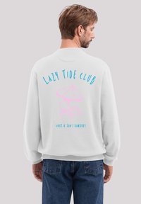White sweatshirt featuring "LAZY TIDE CLUB" in blue and pink lettering with a beach chair and umbrella graphic on the back. Relaxed fit.